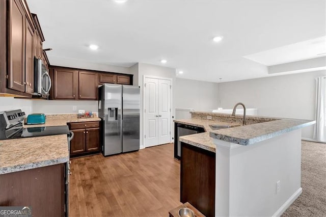 kitchen featuring sink, light hardwood / wood-style flooring, appliances with stainless steel finishes, dark brown cabinetry, and a center island with sink