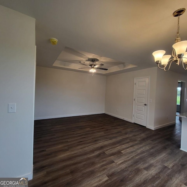 unfurnished room featuring dark wood-type flooring, ceiling fan with notable chandelier, and a tray ceiling