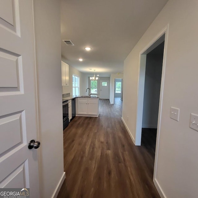 corridor with an inviting chandelier, dark hardwood / wood-style flooring, and sink