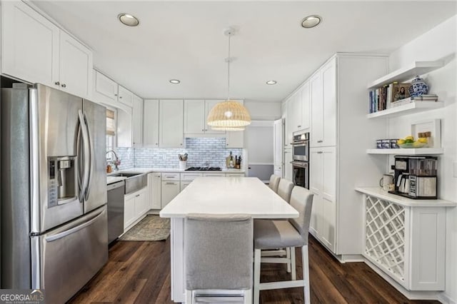 kitchen with pendant lighting, appliances with stainless steel finishes, white cabinetry, a center island, and a kitchen bar