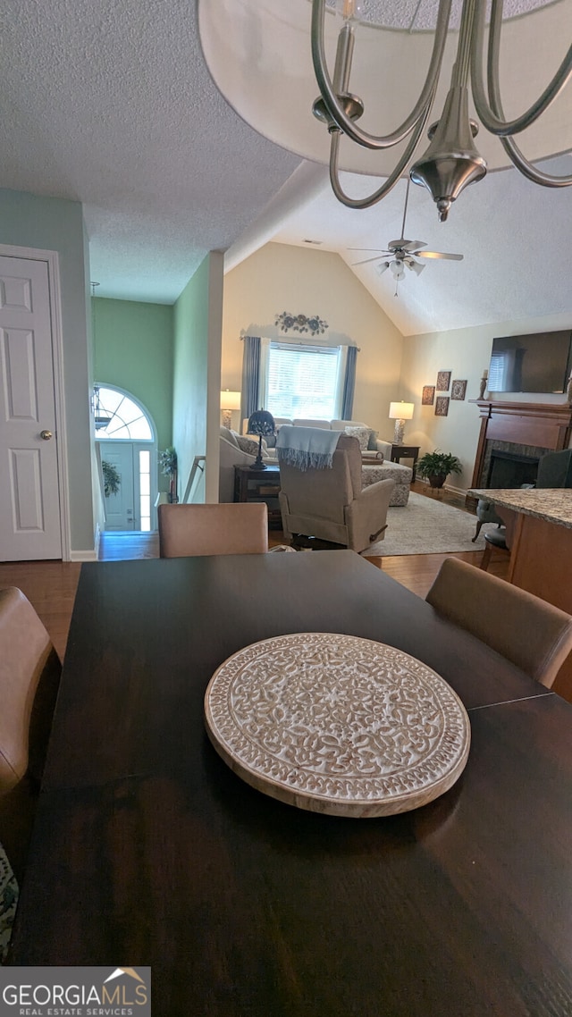 dining space featuring ceiling fan, wood-type flooring, vaulted ceiling, and a textured ceiling