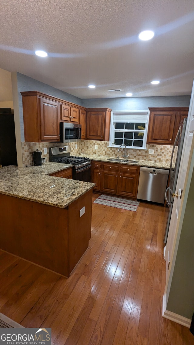 kitchen featuring sink, light hardwood / wood-style flooring, appliances with stainless steel finishes, light stone counters, and kitchen peninsula