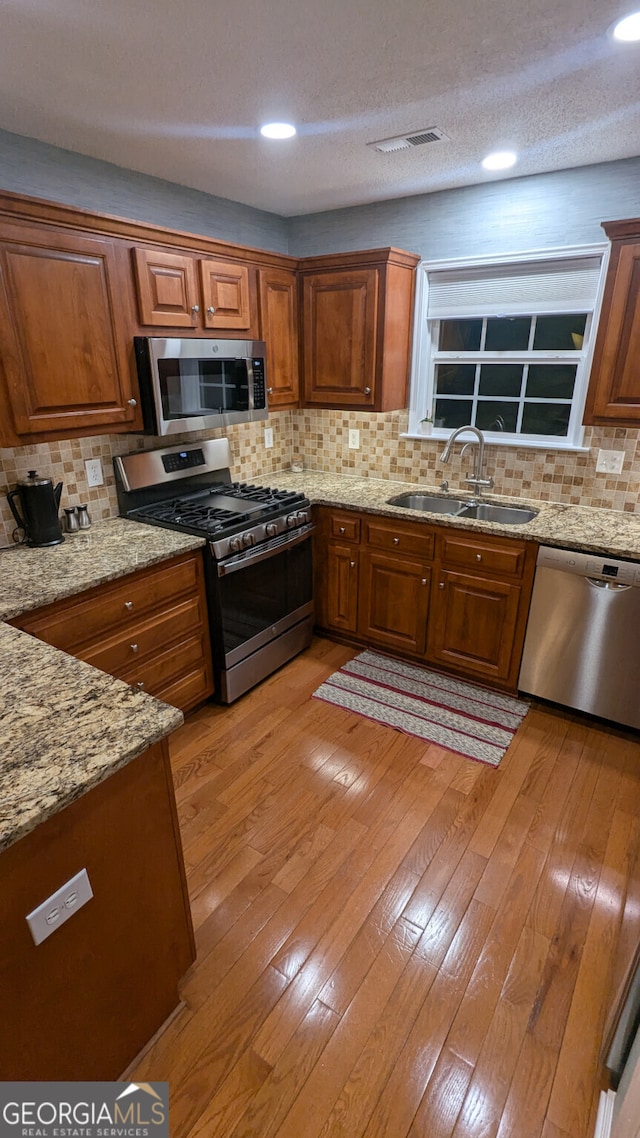 kitchen with appliances with stainless steel finishes, sink, decorative backsplash, light stone counters, and light wood-type flooring