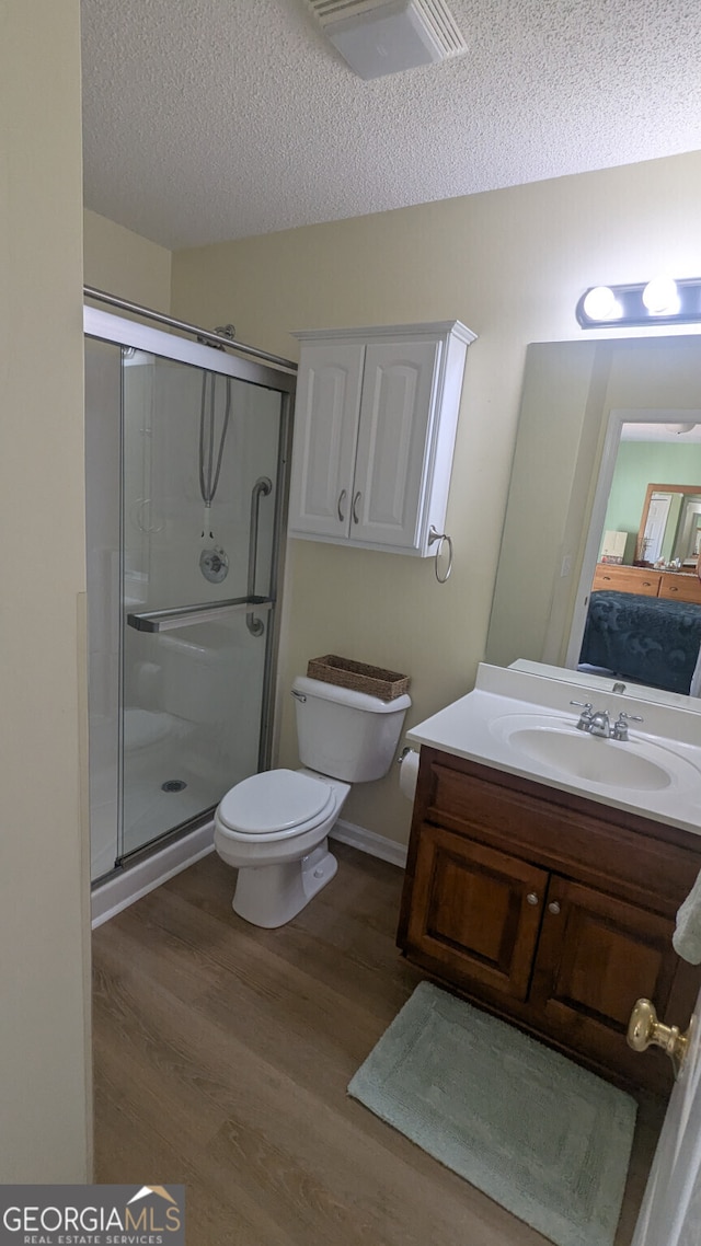 bathroom featuring toilet, a shower with shower door, hardwood / wood-style floors, and a textured ceiling