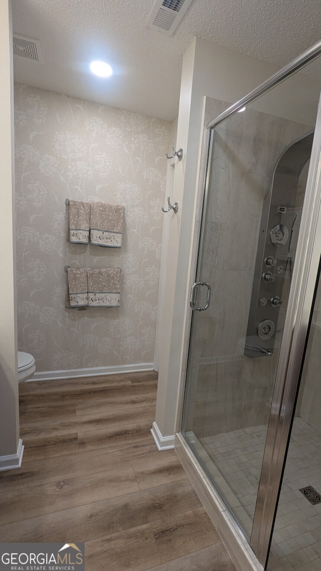 bathroom with wood-type flooring, toilet, an enclosed shower, and a textured ceiling