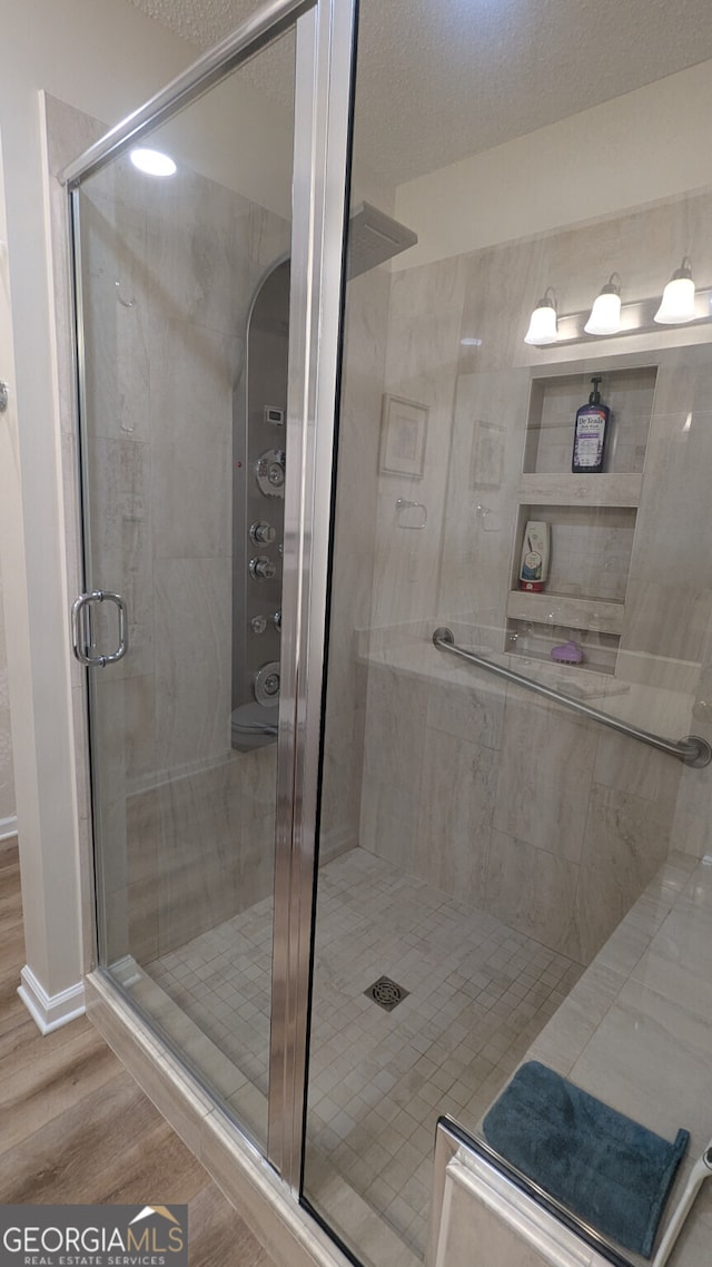 bathroom with wood-type flooring, an enclosed shower, and a textured ceiling