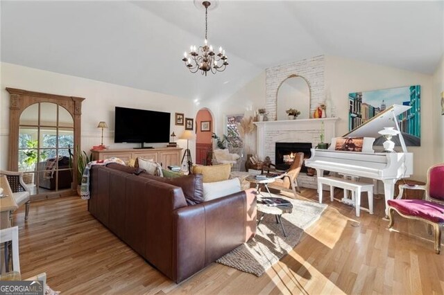 living room featuring an inviting chandelier, lofted ceiling, a fireplace, and light hardwood / wood-style flooring