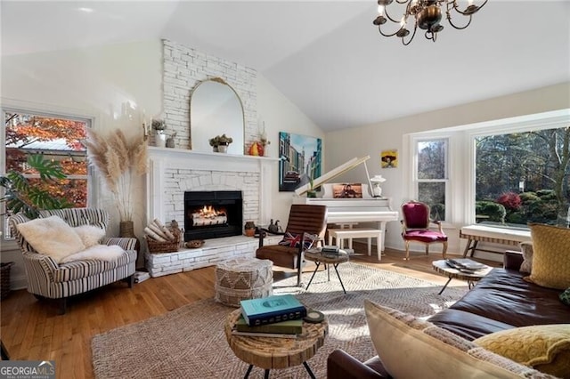 living room featuring vaulted ceiling, wood-type flooring, a notable chandelier, and a fireplace