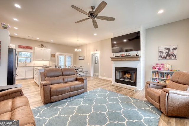 living room with a fireplace, ceiling fan with notable chandelier, and light hardwood / wood-style flooring