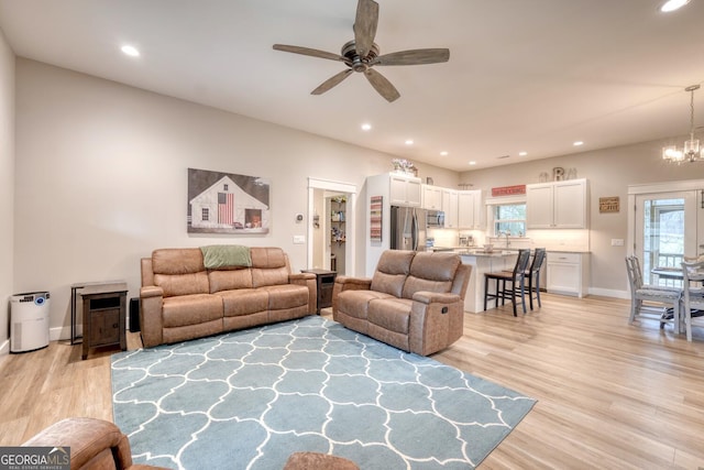 living room featuring sink, ceiling fan with notable chandelier, and light wood-type flooring