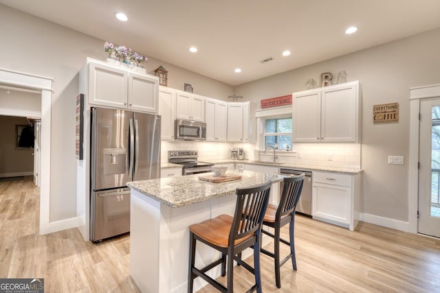 kitchen featuring a kitchen bar, light stone counters, appliances with stainless steel finishes, a kitchen island, and white cabinets