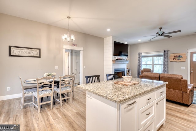 kitchen with white cabinetry, a large fireplace, a kitchen island, decorative light fixtures, and light wood-type flooring