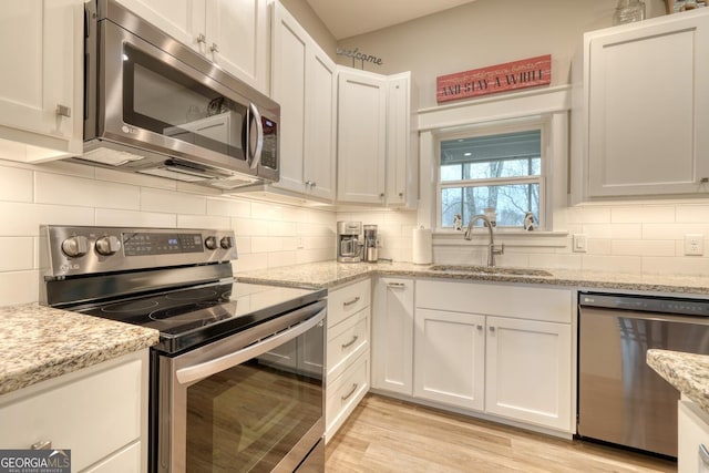 kitchen with sink, light stone countertops, white cabinets, and appliances with stainless steel finishes