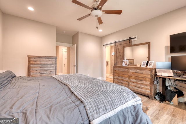 bedroom with ceiling fan, a barn door, and light hardwood / wood-style floors