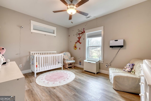 bedroom featuring a nursery area, ceiling fan, radiator heating unit, and light hardwood / wood-style flooring