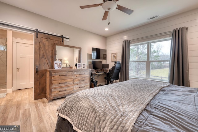 bedroom with ceiling fan, a barn door, light hardwood / wood-style floors, and wood walls