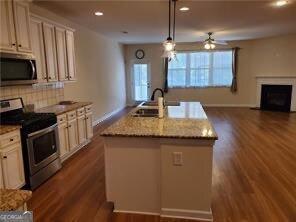 kitchen with sink, a kitchen island with sink, hanging light fixtures, stainless steel appliances, and light stone countertops