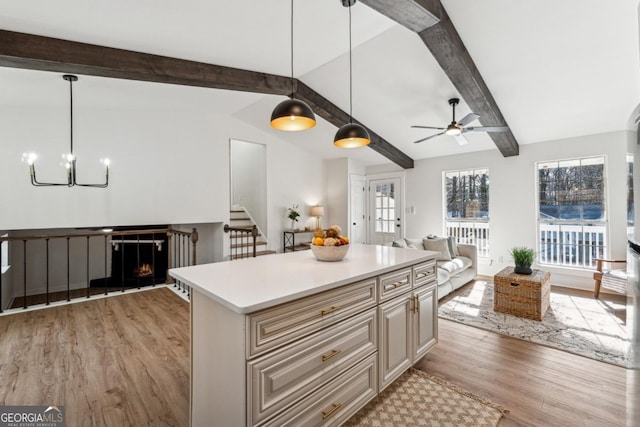 kitchen featuring light hardwood / wood-style flooring, hanging light fixtures, vaulted ceiling with beams, a center island, and ceiling fan with notable chandelier