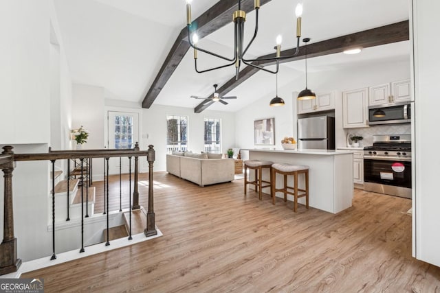 kitchen with a kitchen island, appliances with stainless steel finishes, pendant lighting, lofted ceiling with beams, and white cabinetry