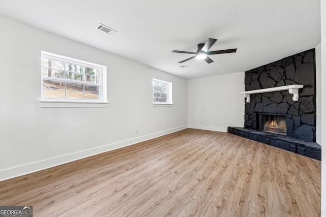 unfurnished living room featuring ceiling fan, a stone fireplace, and light hardwood / wood-style floors