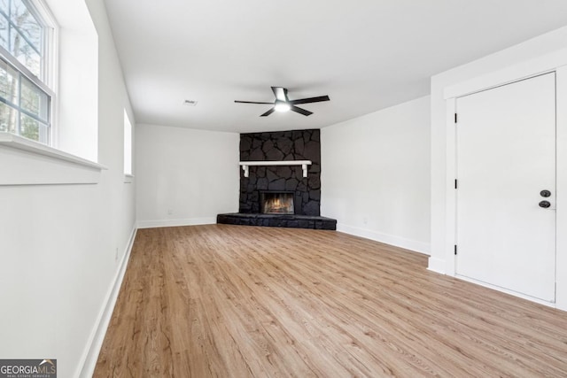 unfurnished living room featuring ceiling fan, a stone fireplace, and light hardwood / wood-style floors