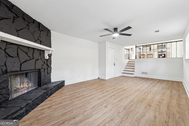 unfurnished living room with ceiling fan, a stone fireplace, and light wood-type flooring