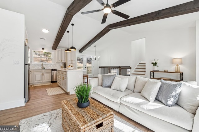 living room with ceiling fan with notable chandelier, sink, lofted ceiling with beams, and light hardwood / wood-style flooring