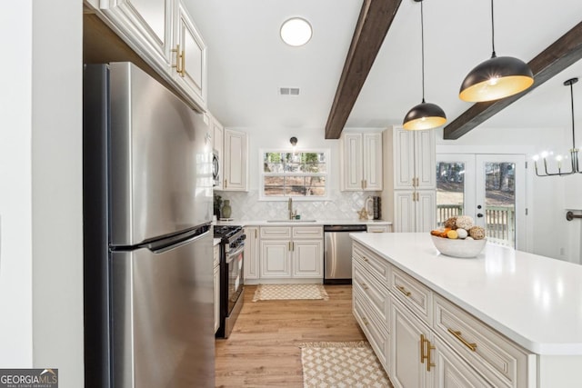 kitchen featuring appliances with stainless steel finishes, white cabinets, and decorative light fixtures