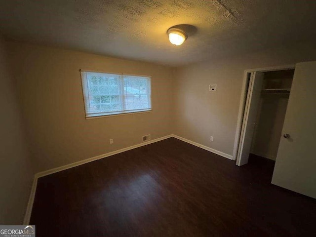 unfurnished bedroom with dark wood-type flooring, a closet, and a textured ceiling