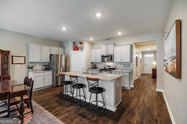 kitchen with sink, white cabinetry, stainless steel appliances, light stone countertops, and an island with sink