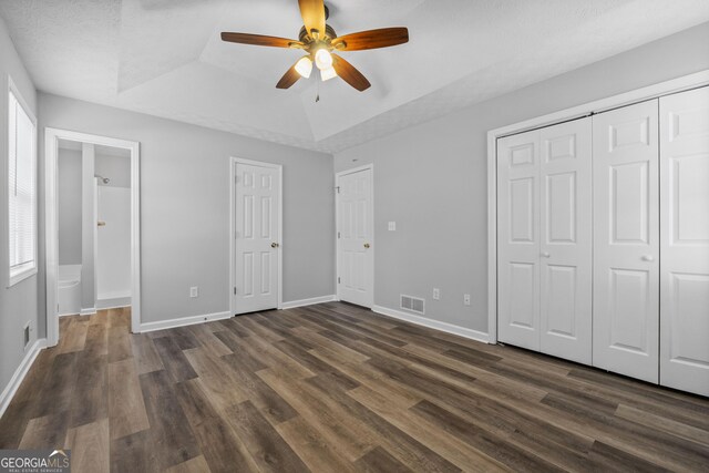 unfurnished bedroom featuring dark wood-type flooring, ceiling fan, ensuite bathroom, and a raised ceiling