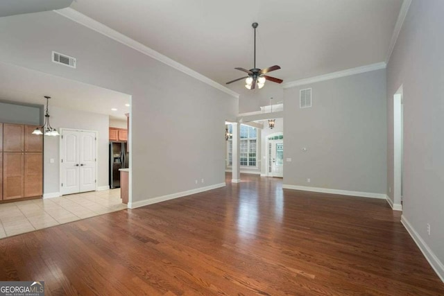 unfurnished living room with crown molding, a towering ceiling, ceiling fan with notable chandelier, and light hardwood / wood-style floors