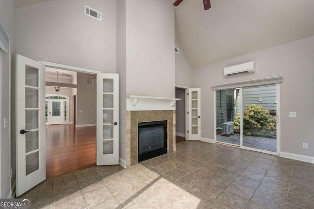 unfurnished living room with a tiled fireplace, an AC wall unit, plenty of natural light, and french doors