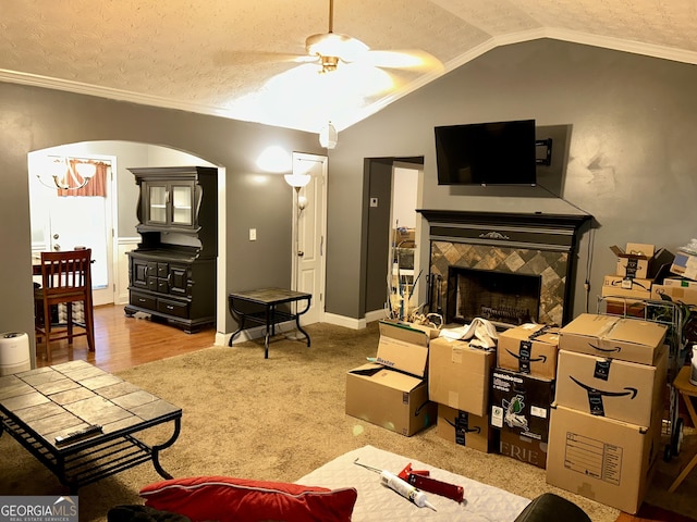 living room featuring crown molding, a tile fireplace, ceiling fan, a textured ceiling, and vaulted ceiling