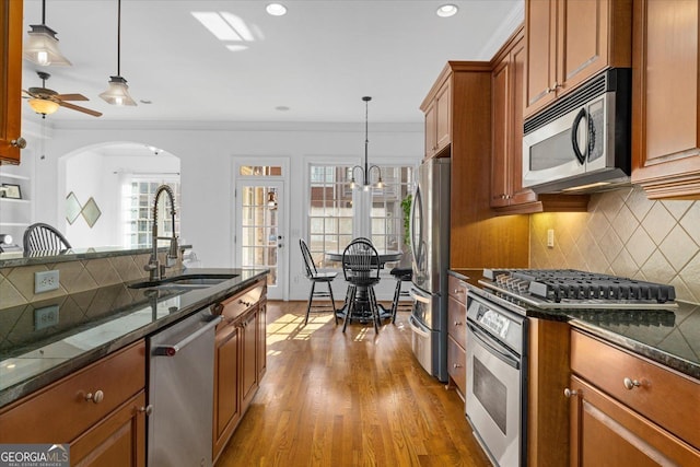 kitchen with appliances with stainless steel finishes, hardwood / wood-style floors, pendant lighting, sink, and dark stone counters