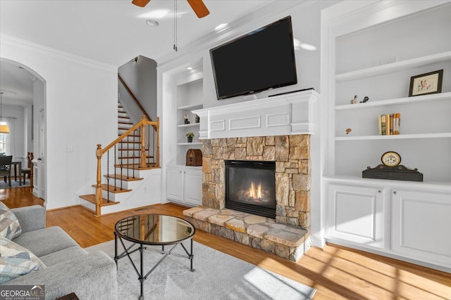 living room with built in shelves, crown molding, ceiling fan, a fireplace, and light hardwood / wood-style floors