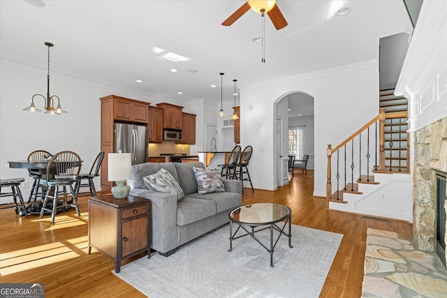 living room with ornamental molding, light wood-type flooring, ceiling fan with notable chandelier, and a fireplace