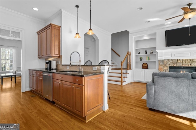 kitchen featuring sink, wood-type flooring, stainless steel dishwasher, ornamental molding, and a fireplace