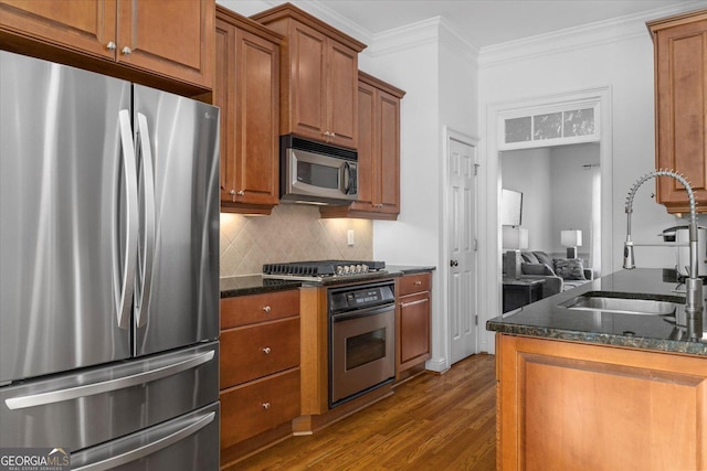 kitchen with sink, crown molding, appliances with stainless steel finishes, dark stone countertops, and dark hardwood / wood-style flooring