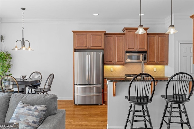 kitchen featuring a breakfast bar, decorative backsplash, hanging light fixtures, stainless steel appliances, and light hardwood / wood-style flooring