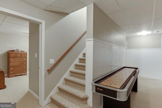 stairs featuring a paneled ceiling and carpet flooring