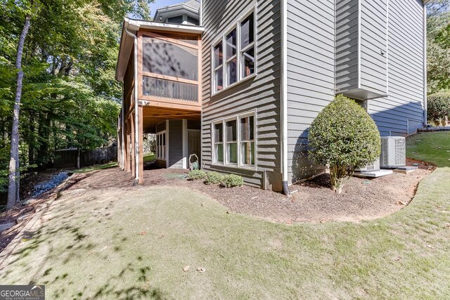 view of home's exterior featuring central AC unit, a sunroom, and a lawn