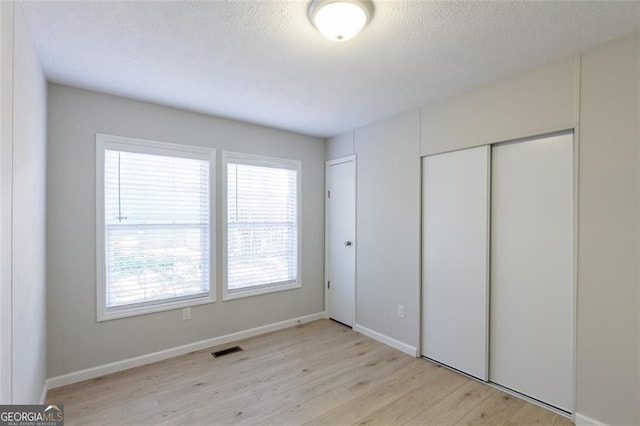 unfurnished bedroom with a textured ceiling, light hardwood / wood-style floors, and a closet