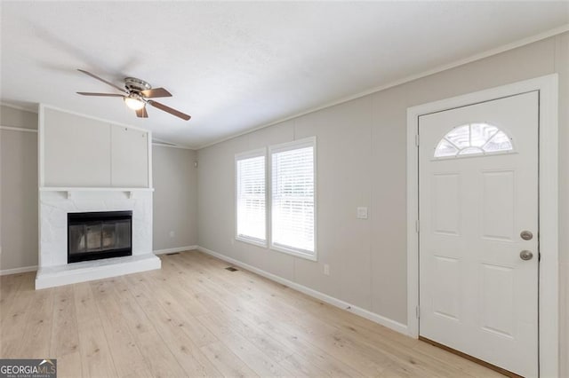 foyer entrance featuring ornamental molding, light wood-type flooring, ceiling fan, and a fireplace