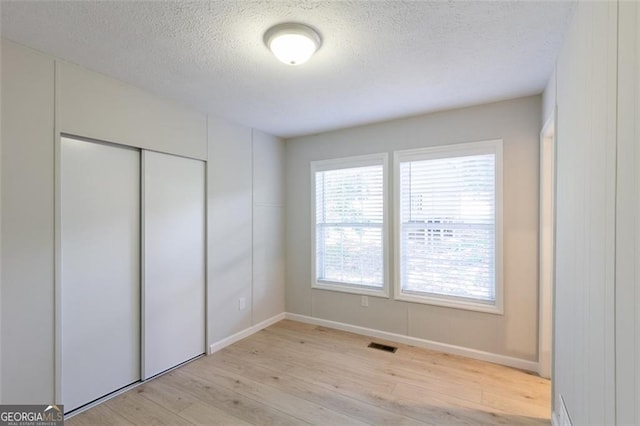 unfurnished bedroom featuring a closet, a textured ceiling, and light wood-type flooring