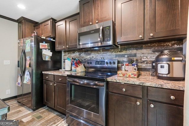 kitchen featuring dark brown cabinets, light wood-type flooring, stainless steel appliances, light stone countertops, and decorative backsplash