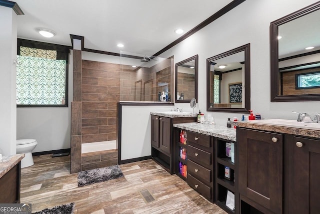 bathroom featuring wood-type flooring, ornamental molding, vanity, tiled shower, and toilet