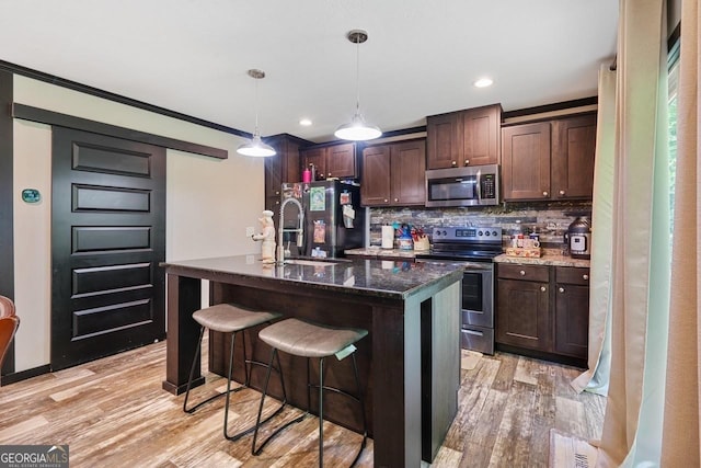 kitchen with sink, appliances with stainless steel finishes, a kitchen island with sink, dark brown cabinetry, and decorative light fixtures