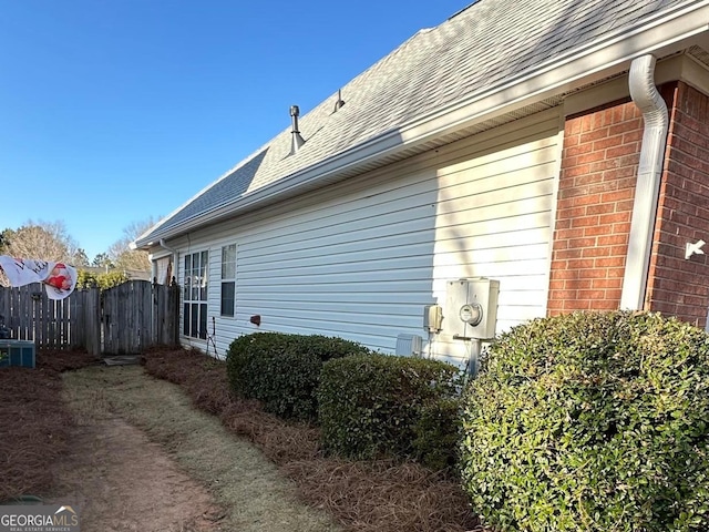 view of property exterior with a shingled roof, fence, and brick siding