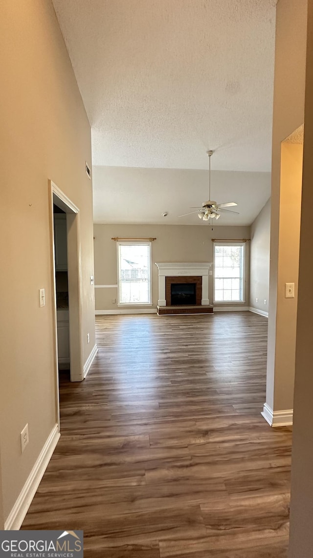 unfurnished living room with a fireplace with raised hearth, lofted ceiling, a textured ceiling, dark wood-style flooring, and a ceiling fan